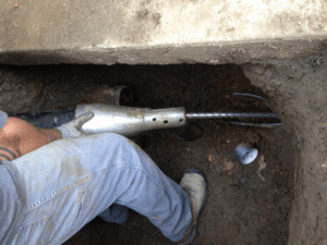 Person in blue jeans holding a white PVC pipe section inside an underground drainage or sewage pit for inspection or repair work.
