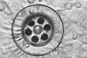 Close-up view of a drain opening surrounded by water droplets and bubbles on a wet surface.