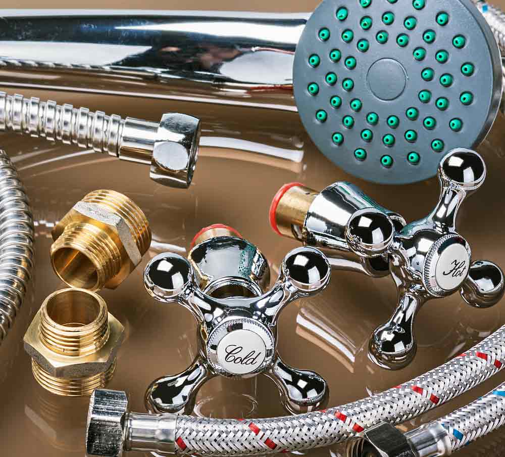 Chrome and brass plumbing fixtures including hot and cold water valve handles, shower head with green spray jets, and flexible hoses on display.