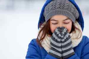Young child wearing a blue jacket, gray knit beanie, and striped neck warmer smiling outdoors in snowy weather.