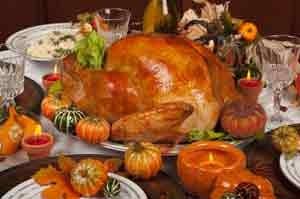 Roasted turkey centerpiece surrounded by autumn decorations, pumpkins, gourds, and place settings on a formal dining table.