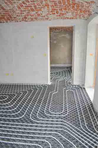 Underfloor heating pipes laid in curved patterns on concrete floor in empty room with exposed brick ceiling.