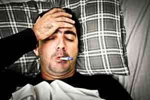 Man lying on checkered pillow holding forehead with hand, appearing to have a headache or migraine.