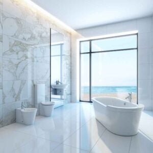 Contemporary bathroom featuring white marble tiles, freestanding soaking tub, glass shower enclosure, and ocean view through floor-to-ceiling windows.
