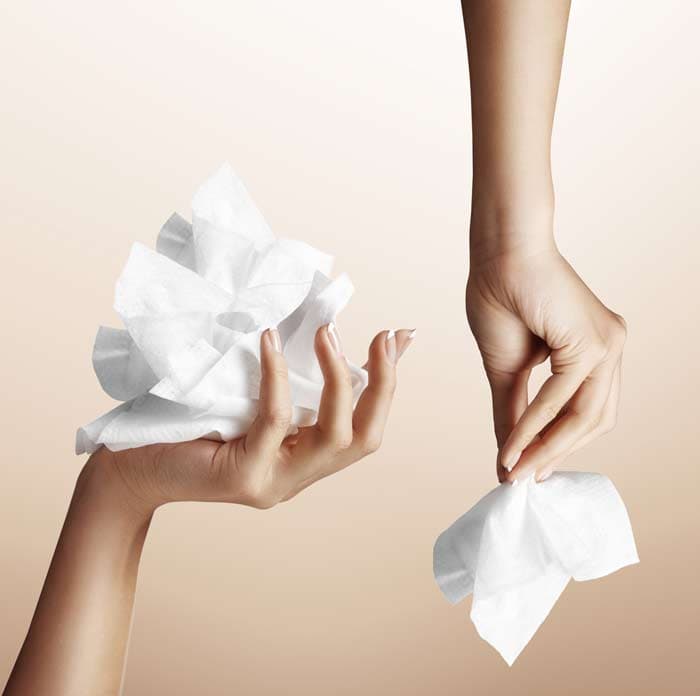 Two hands holding crumpled white wet wipes against a neutral beige background. Demonstrating homemade cleaning product preparation or usage.