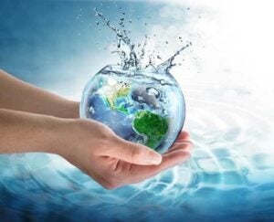 Hand holding a glowing globe with water splash effect against blue sky and ocean water background.