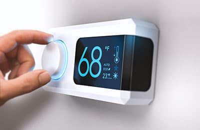 Hand adjusting a white smart thermostat showing 68°F temperature setting with digital display and climate control icons.
