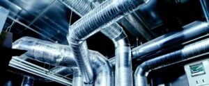 Complex network of shiny metallic air ducts and pipes interconnected with various angles and bends in an industrial ventilation system.