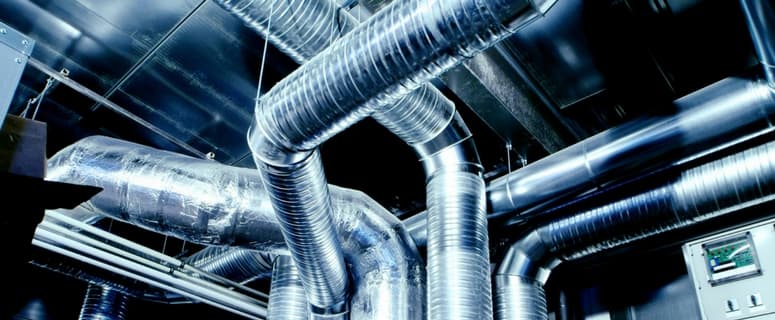 Complex network of shiny metallic air ducts and pipes interconnected with various angles and bends in an industrial ventilation system.