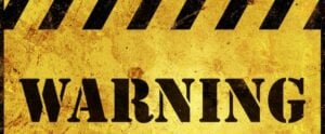 Yellow and black striped warning sign with bold black text reading WARNING on weathered surface.