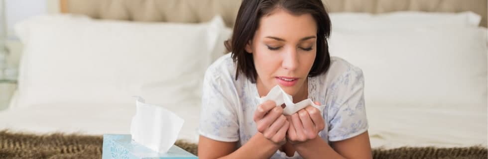 Woman sitting on couch blowing her nose with a tissue during spring allergy season.