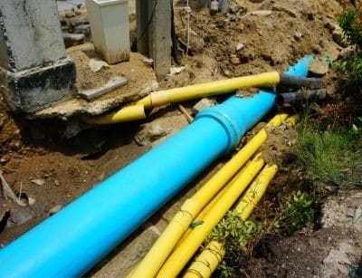 Blue and yellow plastic pipes laid in excavated trench during underground utility installation work.