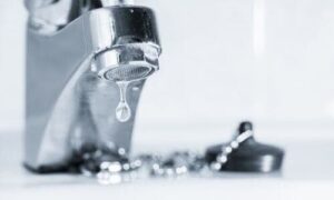 Close-up of a dripping chrome faucet with a water droplet falling, illustrating water waste and plumbing issues.