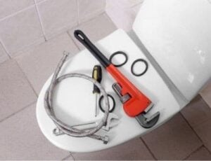 Pipe wrench, adjustable wrench, hose clamps, and flexible supply line arranged on a white toilet tank.
