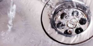 Close-up view of a ceiling or wall drain with water flowing and debris visible inside the circular drain opening.