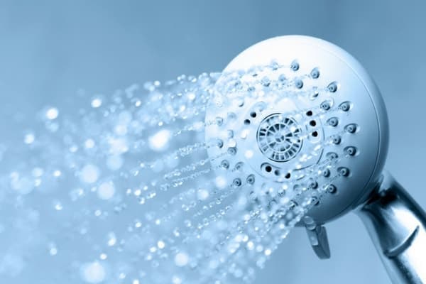 White circular shower head spraying water droplets against a blue background.