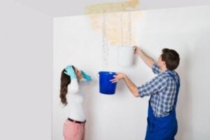 Two people collecting water from ceiling leak into buckets during home water damage inspection and repair.
