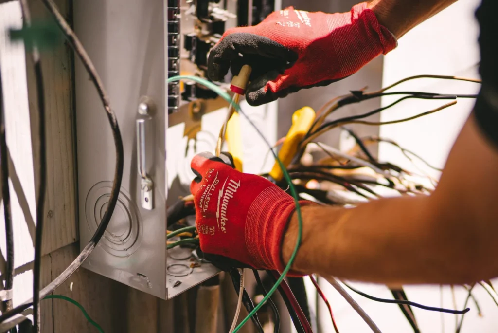 Electrician wearing red work gloves connects colored wires to an electrical panel during installation work.
