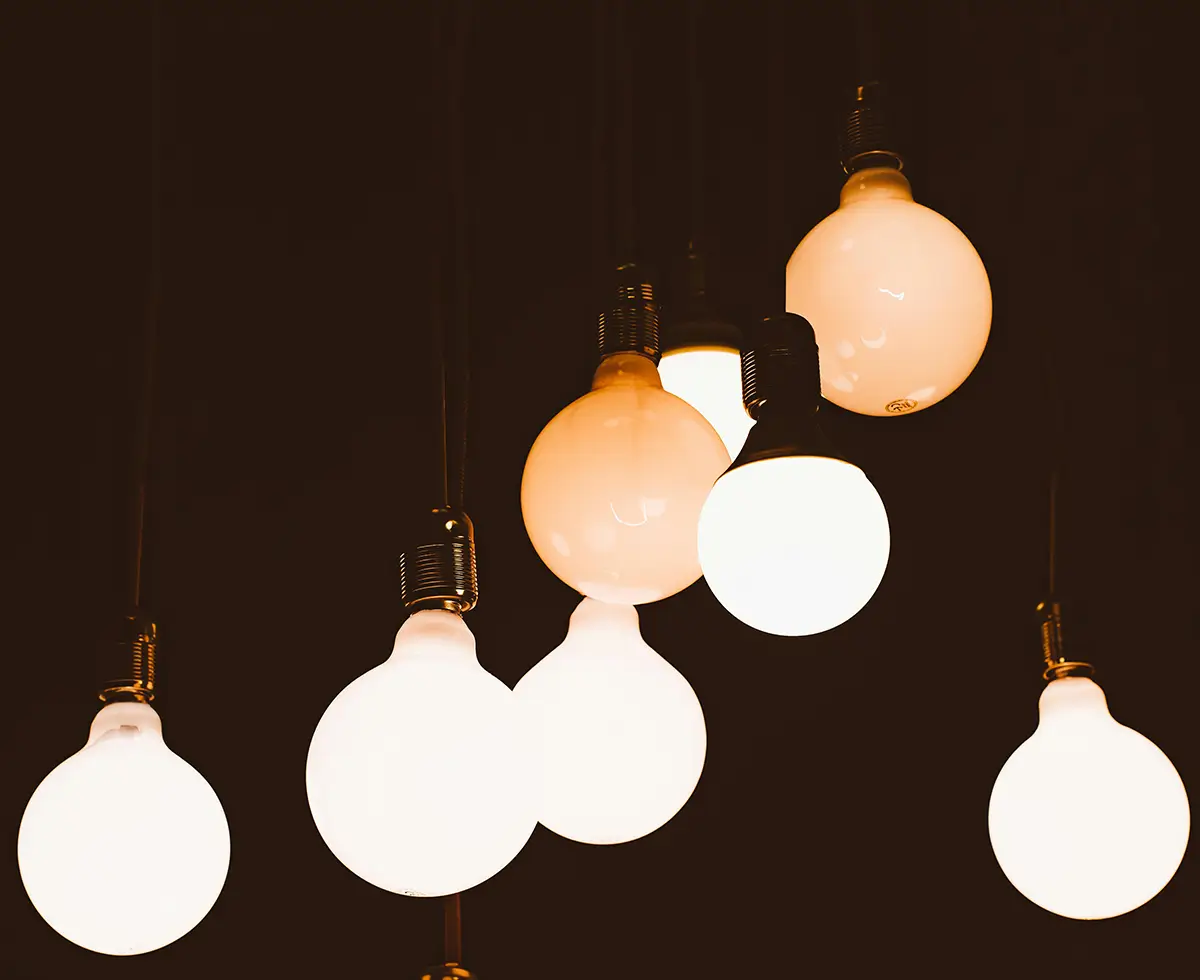 A contemporary pendant light fixture with multiple hanging spherical bulbs in white and warm amber tones against a dark background.