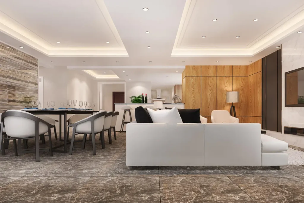 Contemporary open-concept living space featuring white sectional sofa, recessed ceiling lights, wooden accent wall, dining area, and marble flooring.