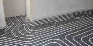 White tubing laid in serpentine pattern on dark matting for radiant floor heating system installation.