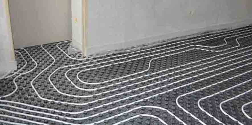 White tubing laid in serpentine pattern on dark matting for radiant floor heating system installation.