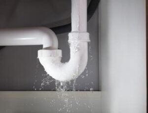 White PVC pipes with water actively leaking and dripping down onto a surface below, showing plumbing failure and water damage.