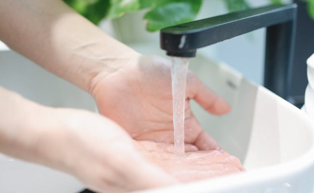 Hand under a black touchless faucet with water flowing into a white sink basin.