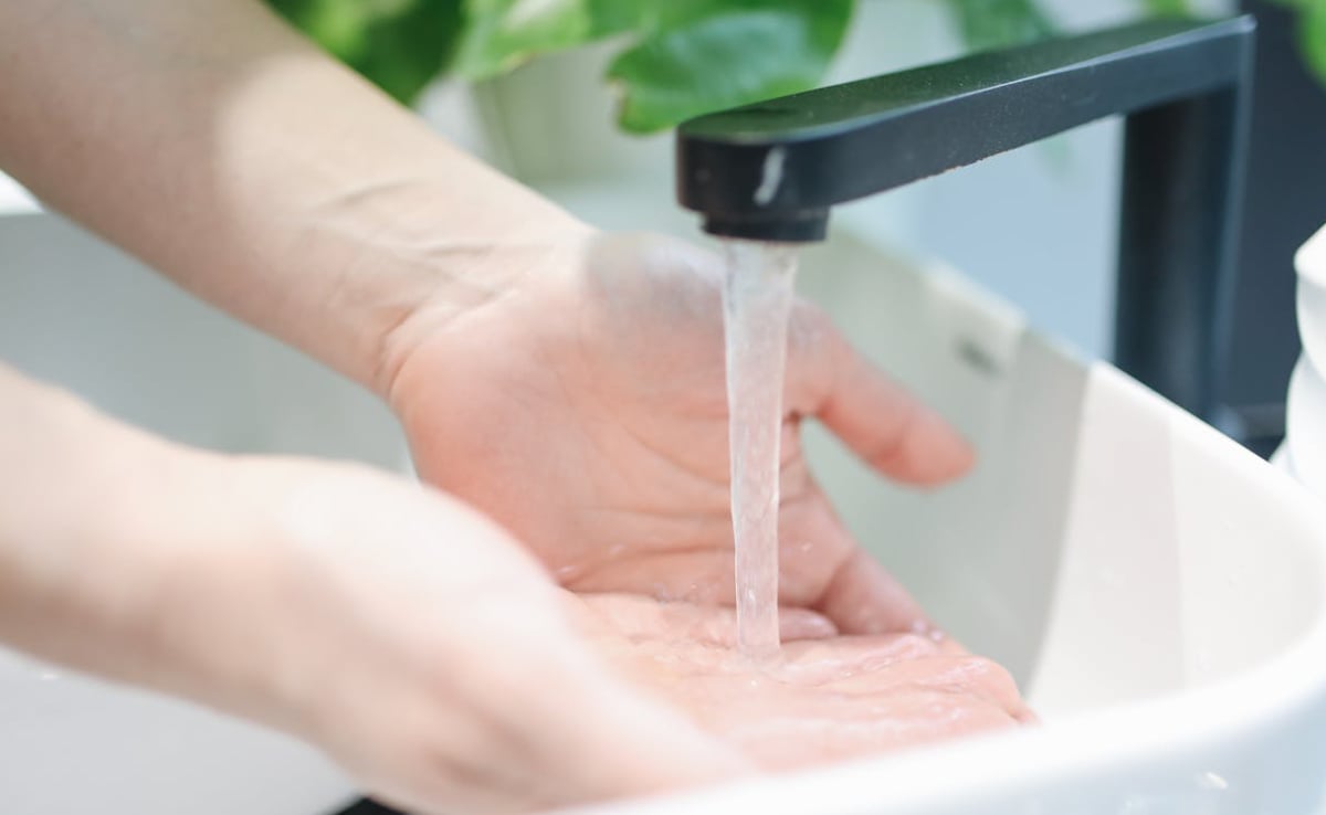 Hand under a black touchless faucet with water flowing into a white sink basin.