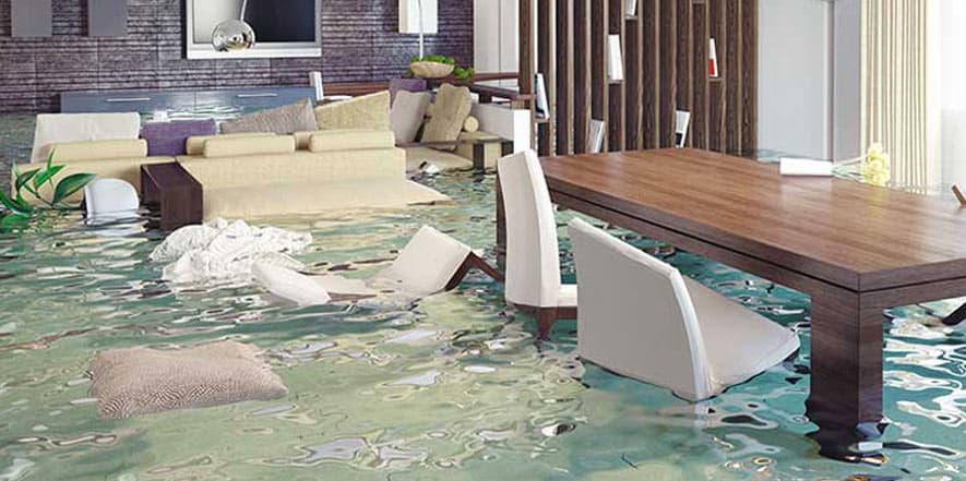 Flooded living room with water covering the floor, submerged furniture, wooden dining table, and cream-colored chairs in a residential home.