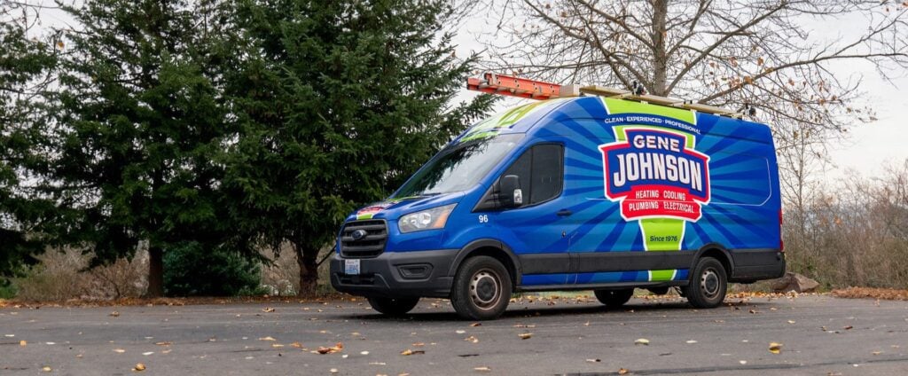 Blue and neon green Gene Johnson service van parked on asphalt with bare trees and evergreens in background.