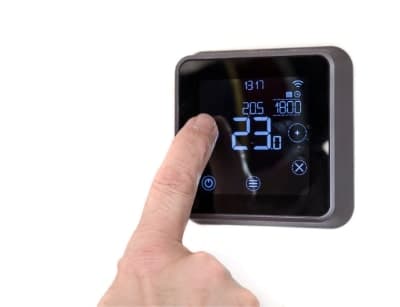 Person's finger touching a digital programmable thermostat display showing temperature settings of 23°C and 21°C with blue LED readout.