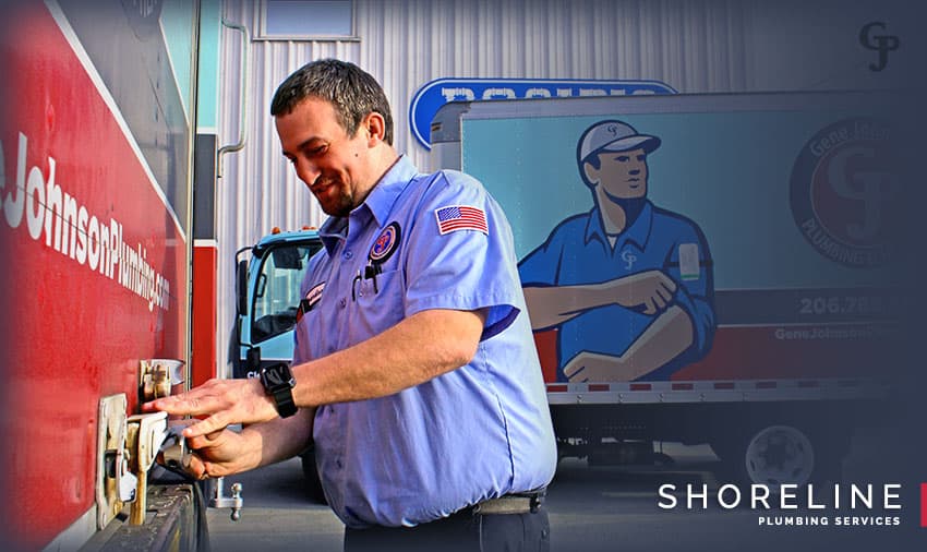 A uniformed plumber in a blue shirt with an American flag patch works on electrical equipment on a red vehicle for Shoreline Plumbing Services.