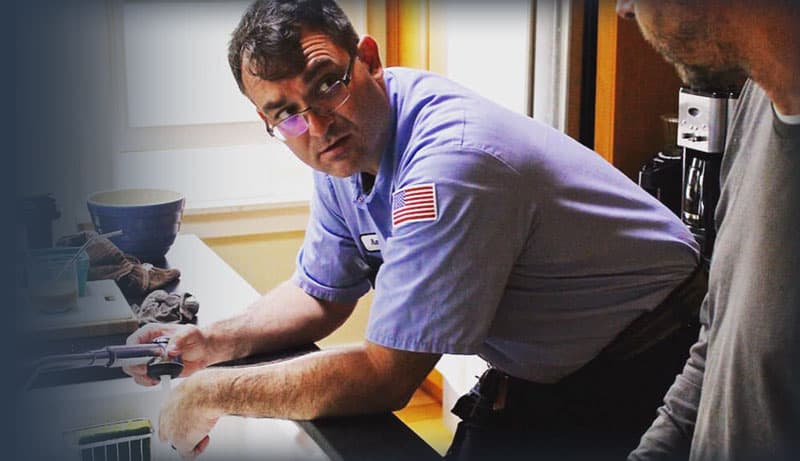 TSA officer wearing blue uniform and glasses inspects a shower tub during security screening at airport checkpoint.